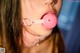 A woman with a pink ball gag in her mouth.