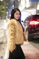 A woman in a fur coat standing on a city street.