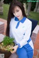 A woman in a white shirt and blue pants holding a potted plant.