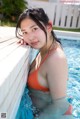 A woman in an orange bikini leaning against a wall in a pool.