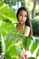 A woman in a red bikini posing in front of some green leaves.