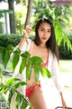 A woman in a red bikini posing in front of a plant.