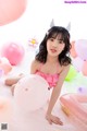 A young girl in a pink bikini sitting on the floor surrounded by balloons.