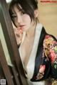 A woman in a black and white kimono leaning against a wooden door.