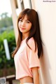 A woman in a pink shirt leaning against a wall.