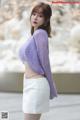 a woman in a purple sweater and white skirt posing for a picture