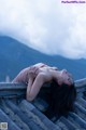 A woman laying on top of a roof with mountains in the background.