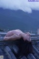 A woman laying on the roof of a building with mountains in the background.