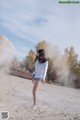 A woman in a white shirt and blue shorts kicking a dust cloud.