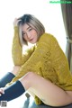 A woman sitting on top of a couch wearing a yellow sweater.