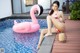 A woman in a bikini sitting next to a pool with a pink flamingo.