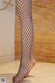 A woman wearing fishnet stockings standing on a tiled floor.