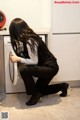 A woman crouching down in front of a washing machine.