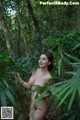 A naked woman standing in the middle of a forest.