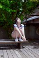 A woman sitting on a wooden bench under a tree.