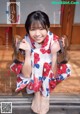 A woman in a kimono sitting on a wooden floor holding a pair of sandals.