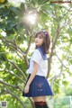 A woman in a school uniform standing in front of a tree.