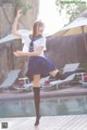 A woman in a school uniform is dancing by a pool.