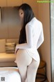 A woman in a white bodysuit is standing on a bed.