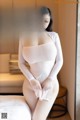 A woman in a white bodysuit sitting on a bed.