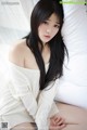 A woman with long black hair sitting on a bed.