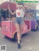 A woman standing in front of a pink and purple carousel.