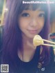 A woman with long purple hair holding chopsticks in her mouth.