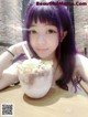 A woman with purple hair sitting at a table with a bowl of ice cream.