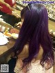 A woman with long purple hair sitting at a table eating food.