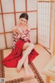 A woman in a red and white kimono sitting on the floor.