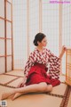 A woman in a red and white kimono sitting on the floor.