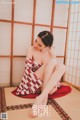 A woman in a red and white kimono sitting on a tatami mat.