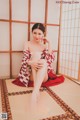 A woman in a red and white kimono sitting on a tatami mat.