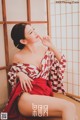 A woman in a red and white kimono sitting on a bed.