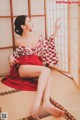 A woman in a red and white kimono sitting on a tatami mat.