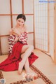 A woman in a red and white kimono sitting on a tatami mat.