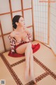 A woman in a red and white kimono sitting on a tatami mat.