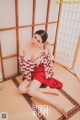 A woman in a red and white kimono sitting on a tatami mat.