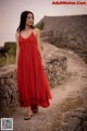 A woman in a red dress standing on a stone wall.