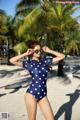 A woman in a blue and white polka dot swimsuit on the beach.