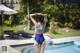 A woman in a bathing suit standing by a swimming pool.