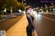 A woman in a black dress standing on a sidewalk at night.