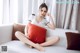 A woman sitting on a white couch with a red pillow.