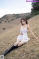 A woman in a white dress and black boots sitting on a hill.