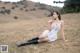 A woman in a white dress and black boots sitting in a field.