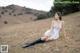 A woman in a white dress and black boots sitting on a grassy hill.