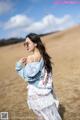 A woman in a white dress and denim jacket standing in a field.