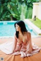 A woman in a pink dress sitting by a swimming pool.