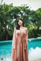 A woman in a pink dress standing by a swimming pool.