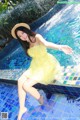 A woman in a yellow dress sitting on the edge of a pool.